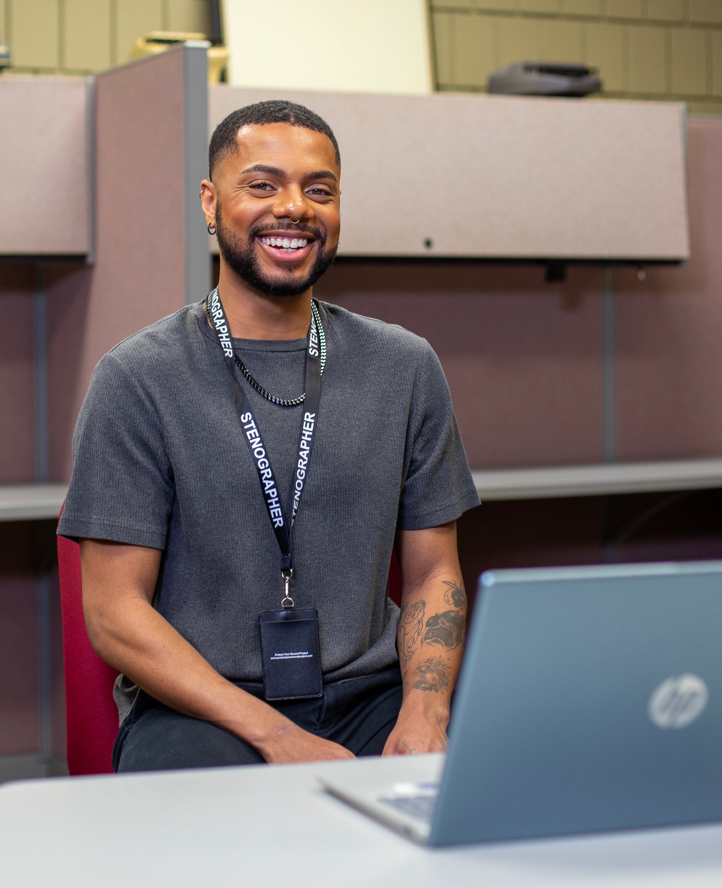Individual seated behind laptop, smiling directly at camera.